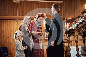 a priest blesses a woman with her daughters in an Orthodox church after a festive church mass