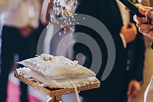 Priest blessing silver wedding rings on silk pillow with holy water for matrimony in church. Wedding spiritual ceremony. Wedding