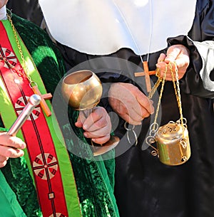 priest with cassock and aspergillum while performing the blessing also with holy water and incense