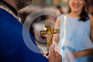 A priest holding a golden cross in front of the family mother. Children baptism and christenings photo