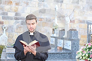 Priest with holy bible in a cemetery