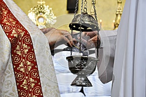The priest places incense inside the thurible that the acolyte holds with his hands and, in the background, the Blessed Sacrament