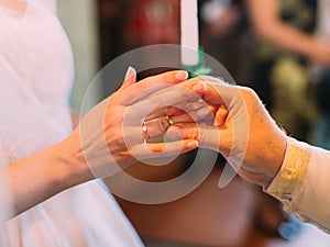 The priest is putting the wedding ring on the hand of the bride.