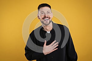 Priest wearing cassock with clerical collar on yellow background