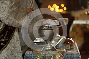 Priests preparing for baptism ceremony. Silver vessel with holy water on stand in church