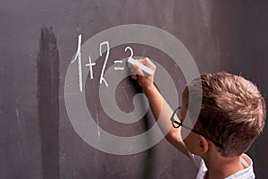 Primary education. Rear view of a schoolboy solves a mathematical example on a blackboard in a math class