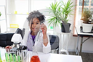 Primary school African curly hair girl does chemistry science experiment in laboratory, cute scientist kid holds chemical test photo