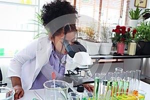 Primary school African curly hair girl looks under microscope, does science experiment in laboratory, cute scientist kid use lab photo