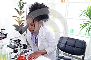 Primary school African curly hair girl looks under microscope, does science experiment in laboratory, cute scientist kid use lab photo