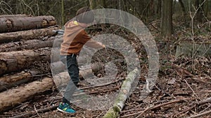 Primary school age boy cuts a log lying on the ground with an ax in the forest.