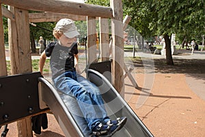 A primary school boy is playing in the playground. The boy sits on a children`s slide. The photo