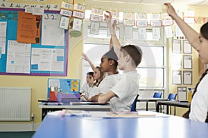 Primary school children raising hands in class, low angle