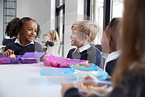 Primary school kids sitting at table eating their packed lunches and talking, close up