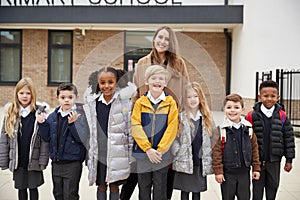 Primary school kids standing in front of school with their teacher looking to camera, front view