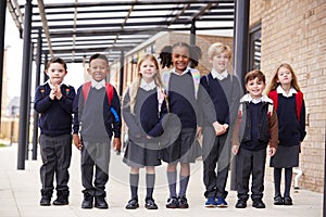 Primary school kids standing in a row on a walkway outside their school, smiling to camera, low angle