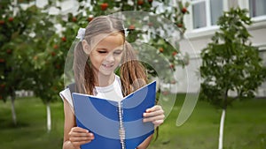 Primary school student with a book in his hands. Girl with a backpack near the school. Beginning of lessons. First day of autumn.