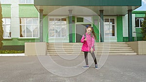 Primary school student. Little girl with a backpack near the building outdoors. Beginning of lessons. First day of autumn