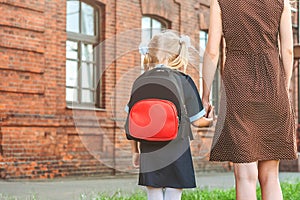 Primary school student and parent go hand in hand. A woman and a young girl with a backpack behind her back. The beginning of the.