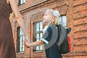 Primary school student and parent go hand in hand. A woman and a young girl with a backpack behind her back. The beginning of the.