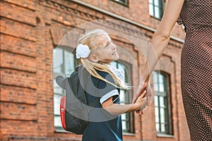 Primary school student and parent go hand in hand. A woman and a young girl with a backpack behind her back. The beginning of the.