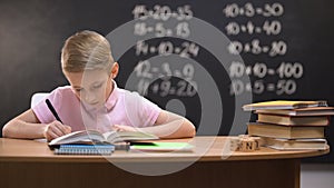 Primary schoolboy writing exercises in notebook, preparing homework, smart kid