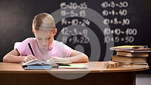 Primary schoolboy writing exercises in notebook, preparing homework, smart kid