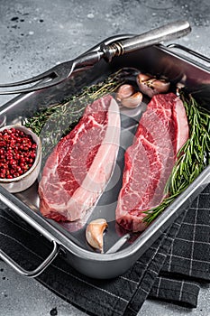 Prime Raw top sirloin beef or cap rump steak in tray with herbs. Gray background. Top view