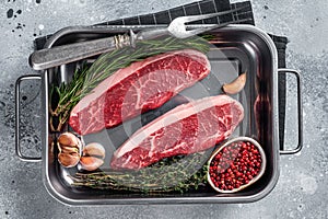 Prime Raw top sirloin beef or cap rump steak in tray with herbs. Gray background. Top view