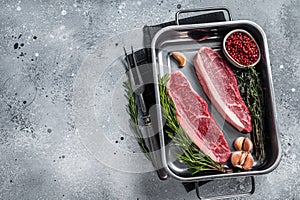 Prime Raw top sirloin beef or cap rump steak in tray with herbs. Gray background. Top view. Copy space