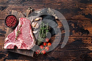 Prime T-bone beef meat steak, raw porterhouse steak on butcher board with herbs. Wooden background. Top view. Copy space