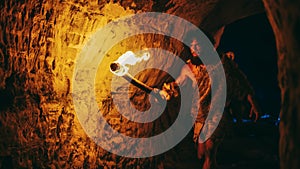 Primeval Caveman Wearing Animal Skin Exploring Cave At Night, Holding Torch with Fire Looking at D