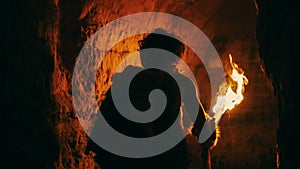 Primeval Caveman Wearing Animal Skin Exploring Cave At Night Holding Torch with Fire Looking at Dr