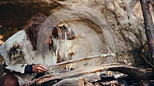 Primeval Caveman Wearing Animal Skin Trying to make a Fire with Bow Drill Method. Neanderthal Kind