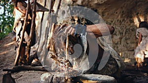 Primeval Caveman Wearing Animal Skin Trying to make a Fire with Bow Drill Method. Neanderthal Kind