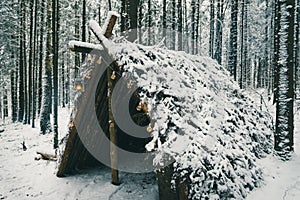 Primitive bushcraft survival shelter with Christmas garland bulbs in winter forest