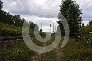 Primitive road along the railway turning to the left among the forest landscape, summer cloudy view.