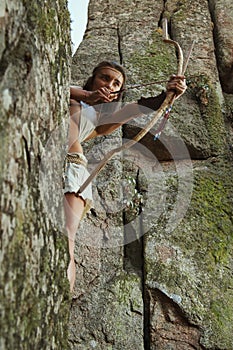 Primitive woman standing on a rock and holding a bow. Amazon woman