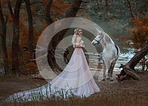 The princess met a unicorn in the forest. The blonde girl with a gentle make-up, is dressed in a long vintage dress with