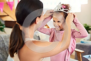 A princess needs her crown. a mother putting a crown on her daughters head during her birthday at home.