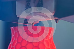 Print head of 3D printer machine printing red flat plastic model - close up