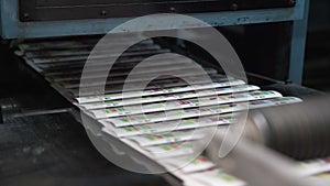 Printed paper newspapers are moved along conveyor. Printing house. Cylinders rotate and move new printed publications