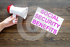 Printed words social security benefits near megaphone on dark wooden background with computer keyboard top view space