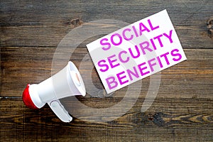 Printed words social security benefits near megaphone on dark wooden background with computer keyboard top view space