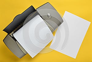 A printer with blank paper forms on a yellow background. Top view, flat lay