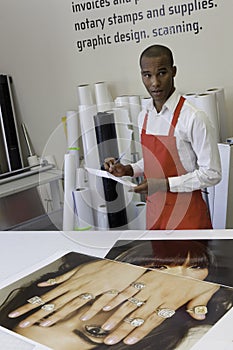 Printing press worker looking away with large print outs on desk