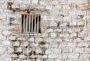 Prison cell window with wooden bars in a white brick wall