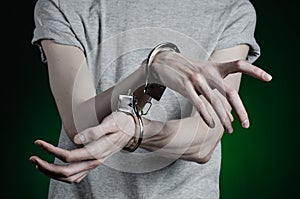 Prison and convicted topic: man with handcuffs on his hands in a gray T-shirt and blue jeans on a dark green background in the stu
