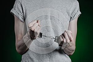Prison and convicted topic: man with handcuffs on his hands in a gray T-shirt and blue jeans on a dark green background in the stu photo