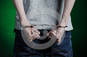 Prison and convicted topic: man with handcuffs on his hands in a gray T-shirt and blue jeans on a dark green background in the stu photo