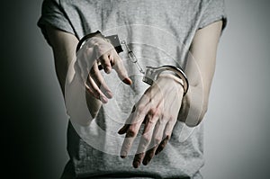 Prison and convicted topic: man with handcuffs on his hands in a gray T-shirt on a gray background in the studio, put handcuffs on